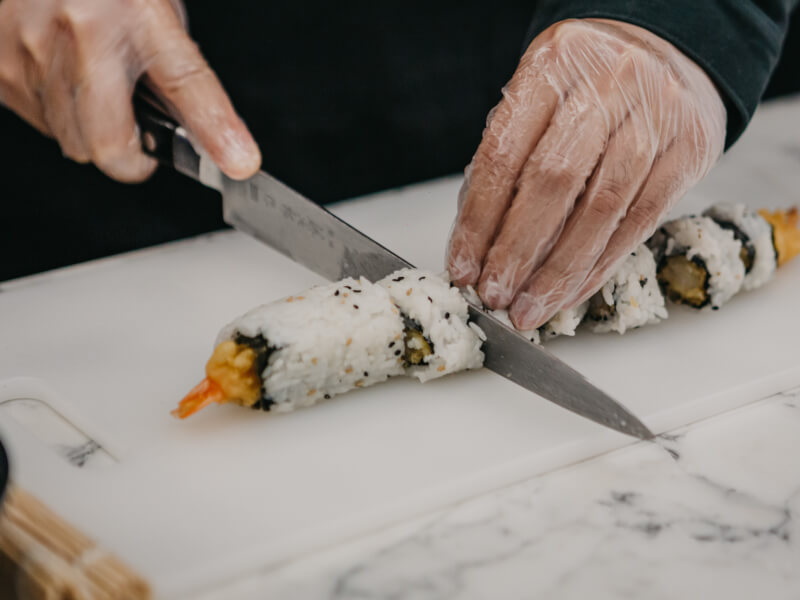 Someone cuts up a roll of sushi.